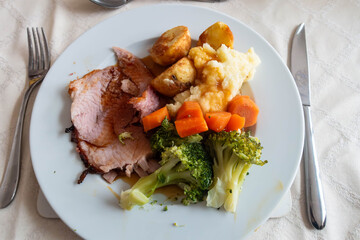 A dinner of home cooked roast gammon with potatoes, broccoli and carrots