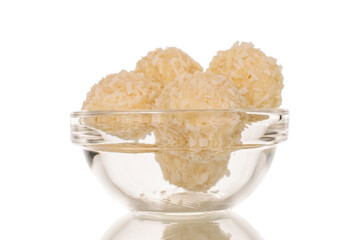 Several candies with nut and coconut shavings in a glass plate, macro, isolated on white background.