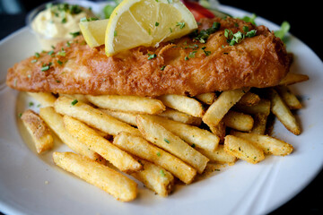 A portion of fried fish and French fries with lemon and chopped green onions on a white plate