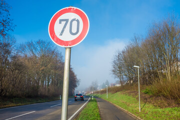 Verkehrsschild 70 km an Einfahrtsstrasse an Ortseingang mit Fahrradweg vor blauem Himmel