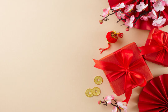 Celebratory presents for the Year of the Dragon. Top view photo of featuring fans, red giftboxes, sakura bloom, gold coins on beige background with promo space