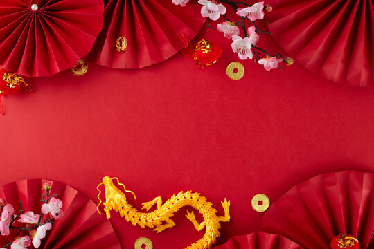 Set the festive mood with Chinese New Year decorations. Top view photo of gold dragon, red paper fans, traditional coins, sakura bloom on red background with advert area