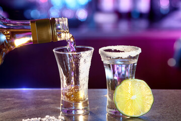 Close-up of a bartender pouring golden tequila into a glass with salt and lime.