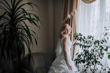 A beautiful happy smiling blonde bride stands in a room indoors near the window. Wedding...