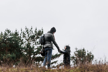 Naklejka na ściany i meble A young woman, a mother and her son, a little boy are walking through the forest in nature holding hands. Photography, portrait, lifestyle, family concept.