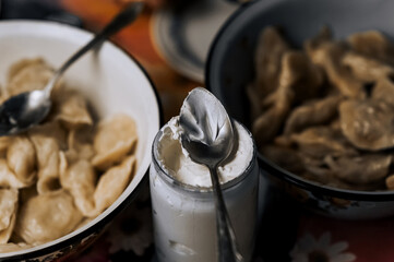 A jar of sour cream, a large bowl of dumplings and a spoon are on the table. Village Ukrainian...