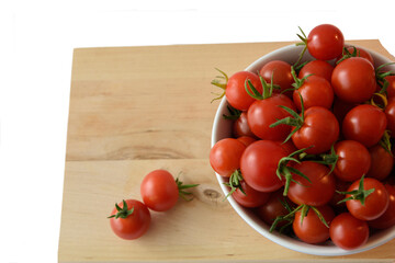 tomatoes in a bowl on a wooden board with two tomatoes besides the bowl, seen in flatlay and transparant background