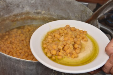 Bowl with hummus dip with chickpea in hand with olive oil and parsley hot pot