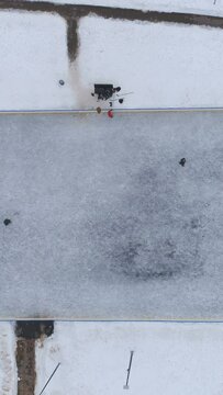 Ice hockey rink in the city park. Players shoot the puck. Aerial view. Flying upward. Vertical Video