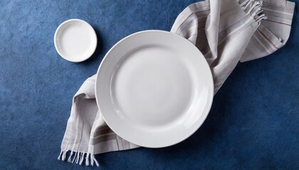 Top view on dark blue background empty round white plate on tablecloth for food	
