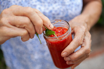 Woman's Hands Finishing Tomato Sauce Glass Recipe with Basil Leaf and Olive Oil Before Sealing it with a Brief Boiling