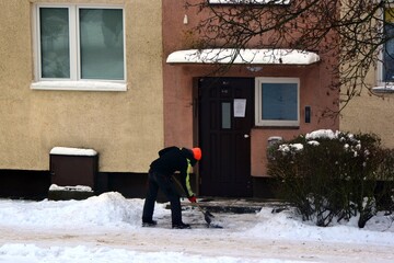 A worker clears snow from the sidewalks of a housing estate in a heavy snowfall winter