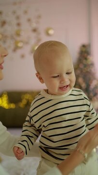 A little boy takes his first steps with his mother supporting him