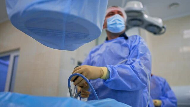 Surgeon using the endoscopic device at operation. Low angle view on the doctor performing minimal invasive surgery.