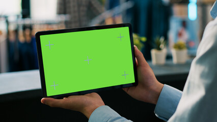 Boutique worker analyzing digital device with chroma key green screen mock up display, working in...
