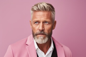 Serious mature man looking at camera with serious expression, standing against pink background