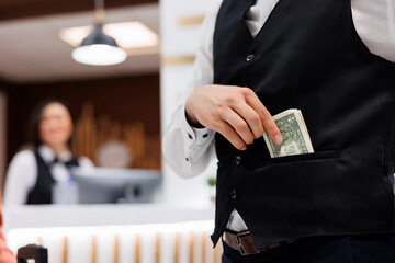 Hotel staff receives money in lobby, putting cash in pocket to help guests with luggage after check...