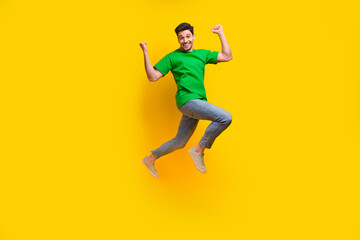 Fototapeta na wymiar Full length photo of ecstatic satisfied man dressed green t-shirt flying raising fists up win betting isolated on yellow color background