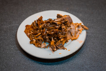 A bunch of leftover meat from chicken and pork on a plate. Meaty leftovers from a dinner on a white plate.