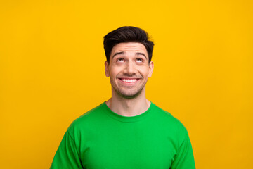 Portrait photo of cheerful guy in green t shirt looks above head novelty proposition customers discount isolated on yellow color background
