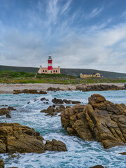 Fototapeta na wymiar Cape Agulhas Lighthouse, southernmost tip of Africa from the ocean with rocks and blue water, L'Agulhas, South Africa