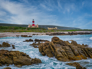 Cape Agulhas Lighthouse, southernmost tip of Africa from the ocean with rocks and blue water,...