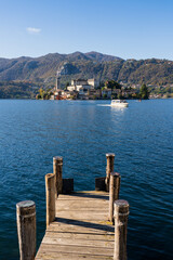 San Giulio Island within Lake Orta in Piedmont, Italy. mountains, boat sailing on blue water, church, monastery, other buildings and pier foreground