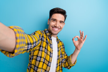 Photo of positive handsome man dressed yellow plaid shirt showing okey gesture tacking selfie...