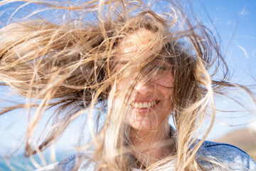 Closeup of young woman face covered with flying hair in windy day. Portrait female with hair...