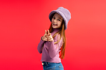 Smiling cheerful little girl wearing stylish purple hat looking at camera, pointing fingers