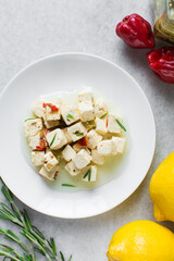 Top view of marinated feta cheese cubes on white plate. Cheese cubes marinating in herbed oil, flat lay of feta cheese in olive oil on plate
