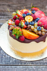 Delicious cheesecake with melted chocolate, apples, strawberries, blueberries, peaches, raspberries and kumquats on the top, rustic background