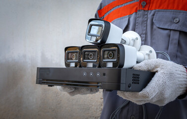 Professional technician wearing gloves holds CCTV camera and video surveillance equipment with wall background. copy space