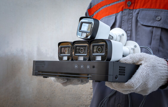 Professional technician wearing gloves holds CCTV camera and video surveillance equipment with wall background. copy space