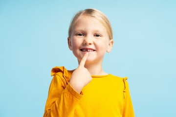 Portrait of little girl wearing casual clothes, pointing finger on teeth. Dental concept, treatment