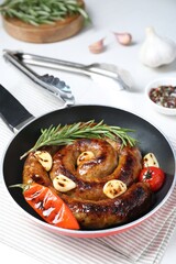 Delicious homemade sausage with garlic, tomato, rosemary and chili in frying pan on table, closeup