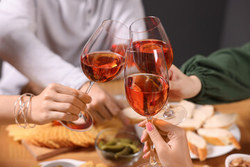 People clinking glasses with rose wine above wooden table, closeup