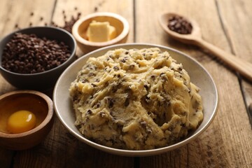 Chocolate chip cookie dough in bowl and ingredients on white wooden table, closeup