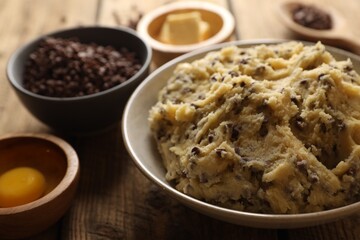 Chocolate chip cookie dough in bowl and ingredients on white wooden table, closeup
