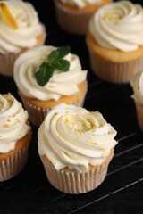 Delicious cupcakes with white cream and lemon zest on cooling rack, closeup