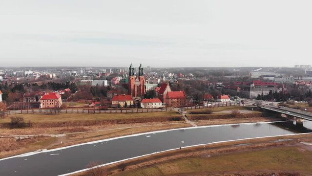 Drone reverse dolly from red Cathedral in Poznan, Poland with snow covered riverbank