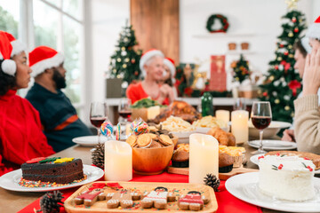 Happy diverse family meeting each other at cozy home for celebrating Christmas or New Year. They hugging, talking and smiling. Setting table with dishes. Holidays decorations and Christmas Tree.
