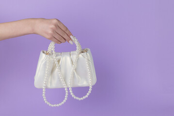 The girl's hand holds a white bag trimmed with pearls on a purple background.