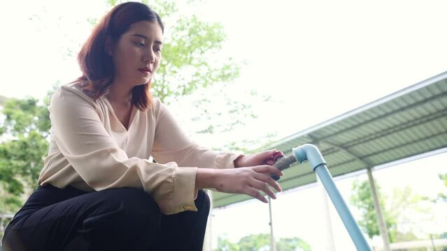 Young asian woman wants to use tap water from an outdoor faucet in hot weather. She sits and turns on the faucet but is upset because the water doesn't flow due to water scarcity in summer.