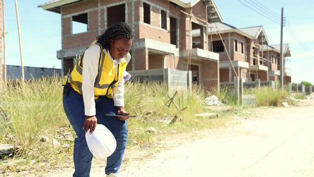 African American female worker inspects construction site working outdoors in excessive heat causing fatigue thirst fainting and discomfort.