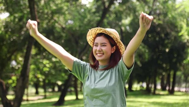 Portrait young asian woman wearing sunny morning hat who is cheerful joyful happy in a good mood assertive positive jumping in a garden with nature shady trees pure air smiling looking at the camera.