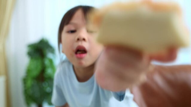 Cheerful small asian girl sits and eats delicious pizza for breakfast. She shows off a slice of pizza in her hand and eats it happily.
