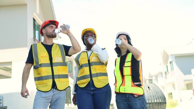 Group of male and female workers of various nationalities on a construction site stood and drank clean distilled water in bottles to quench their thirst with refreshing smiles while taking breaks.