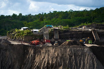 A stone quarry in Indonesia. Large equipment such as bulldozers and dump trucks are working on the site.