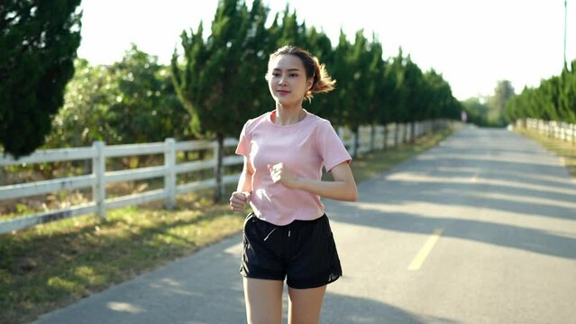 Happy thin woman wearing sports clothes jogging at the park at sunrise Beautiful young Asian woman in exercise clothes running outdoors. Morning exercise The concept of a healthy and active lifestyle